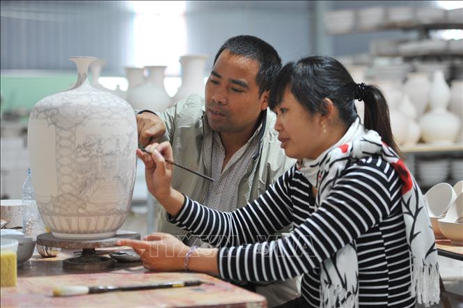 Trong ảnh: Nghệ nhân Phạm Văn Vang hướng dẫn cho thợ mới vẽ lên sản phẩm gốm Bồ Bát. Ảnh: Minh Đức - TTXVN