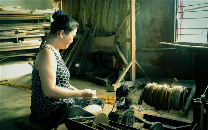 Photo: A craftswoman in Long Dinh village spins sedge fibers into thread for weaving. VNA Photo: Nam Thái