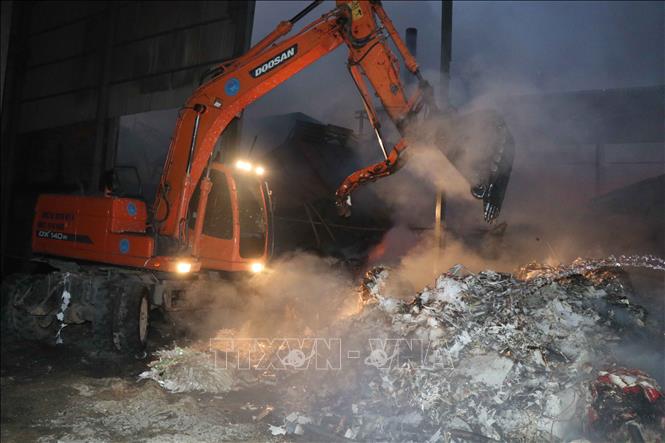 Trong ảnh: Lực lượng PCCC tiến hành cẩu lõi giấy, phun nước, tránh cháy âm ỉ. Ảnh: Thanh Thương  – TTXVN