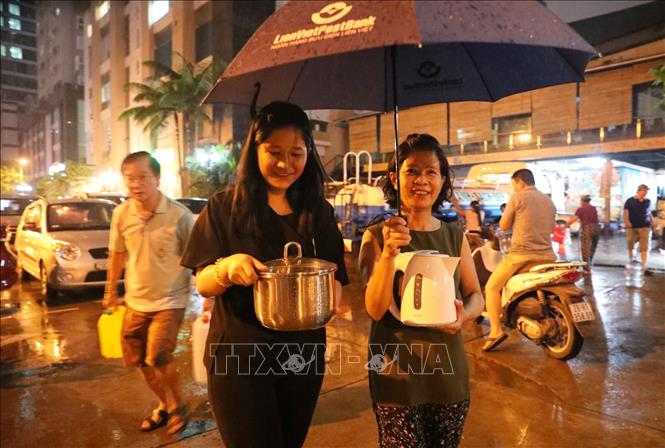 Trong ảnh: Người dân khu đô thị Hapulico (Thanh Xuân Trung) đội mưa mang bình, xô, chậu, thậm chí cả ấm nước lấy nước sạch lúc nửa đêm. Ảnh: Thành Đạt - TTXVN