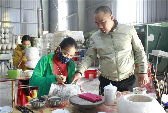 Trong ảnh: Anh Phạm Văn Vang hướng dẫn thợ vẽ trên gốm. Ảnh: Thùy Dung - TTXVN
