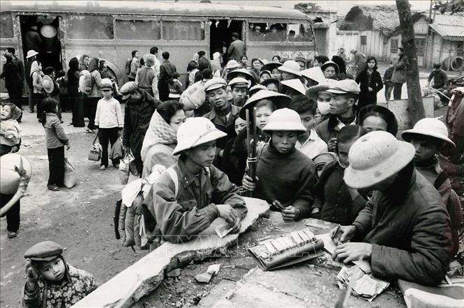 Trong thời kỳ Mỹ dùng không quân đánh phá miền Bắc, trong đó có Hà Nội những năm 1966-1967, quân và dân Thủ đô tiếp tục phát huy tinh thần đoàn kết, thực hiện đúng chủ trương, chỉ đạo của Trung ương để thi đua xây dựng, sản xuất, trở thành hậu phương vững chắc cho tiền tuyến “miền Nam ruột thịt”. Trong ảnh: Cảnh bán vé xe khách ở Hà Nội sau kỳ nghỉ Tết năm 1967. Nhiều trẻ em được đưa về ăn tết tại Hà Nội sẽ theo các chuyến xe trở về vùng sơ tán tại nông thôn. Ảnh: Tư liệu/TTXVN phát