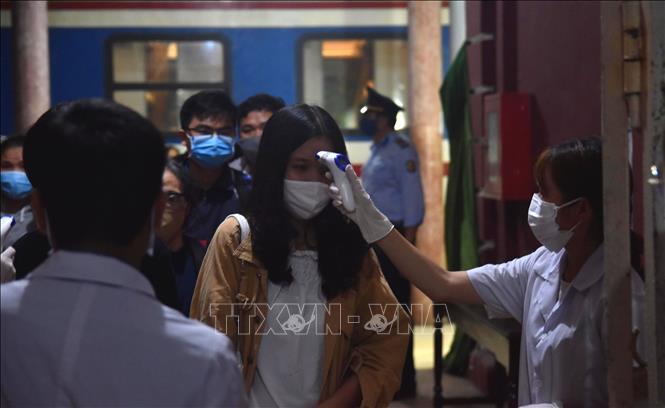 Photo: A student takes passengers’ temperatures at the station. VNA Photo: Tường Vi