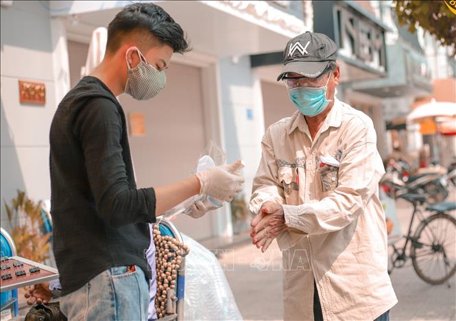 Trong ảnh: Hướng dẫn người bán vé số dạo rửa tay sát khuẩn trước khi nhận quà. Ảnh: Lê Thúy Hằng-TTXVN