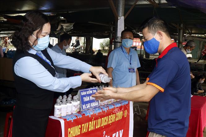 Trong ảnh: Lực lượng chức năng rửa tay sát khuẩn cho người dân tại  tại chợ trung tâm thị trấn Tằng Loỏng. Ảnh: Quốc Khánh - TTXVN