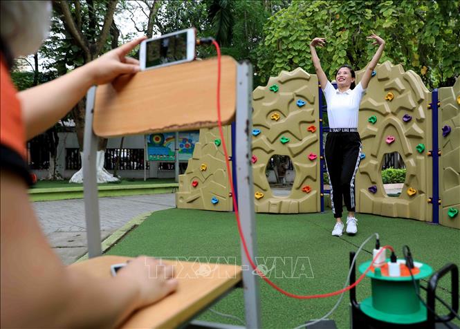 Trong ảnh: Giáo viên trường Mầm non Tràng An, quận Thanh Xuân (Hà Nội) ghi hình bài tập thể dục giúp trẻ tăng cường vận động tại nhà.  Ảnh: Thanh Tùng - TTXVN 