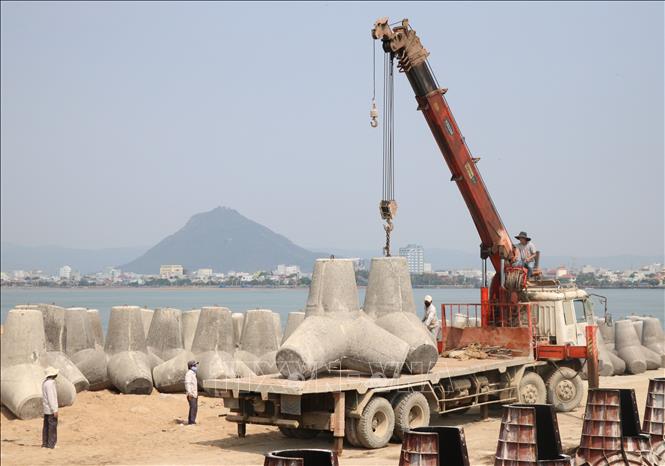 Trong ảnh: Các trụ bê tông chắn sóng nặng hàng tấn được vận chuyển lên xe tải thi công kè Đà Diễn. Ảnh: Phạm Cường - TTXVN
