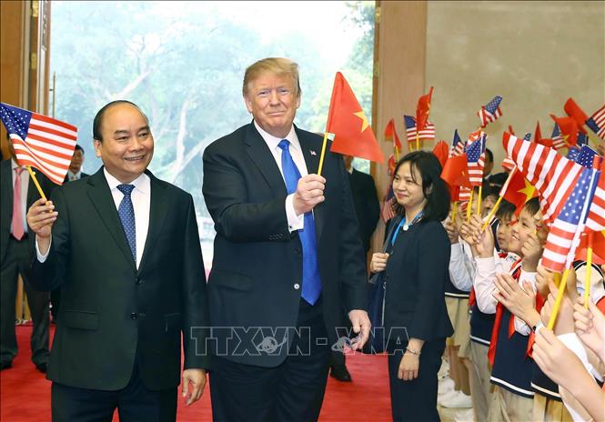 Trong ảnh: Thủ tướng Nguyễn Xuân Phúc và Tổng thống Hoa Kỳ Donald Trump vẫy cờ hai nước cùng với thiếu nhi Hà Nội chào mừng Tổng thống đến Việt Nam, sáng 27/2/2019, tại Trụ sở Chính phủ. Ảnh: Thống Nhất – TTXVN