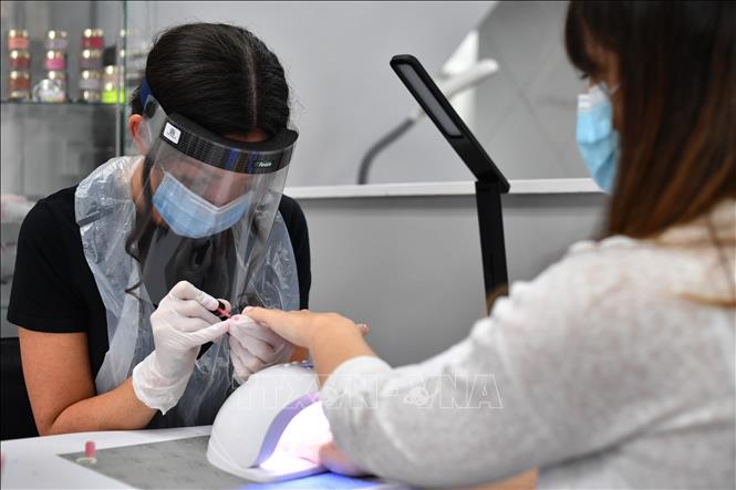Trong ảnh: Một nhân viên đeo tấm chắn nhựa tại một tiệm làm đẹp ở  Oxton, Birkenhead, Anh. Ảnh: AFP/TTXVN