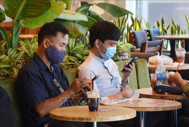 Trong ảnh: Khách hàng đeo khẩu trang khi uống cà phê tại quán. Ảnh: Văn Dũng - TTXVN