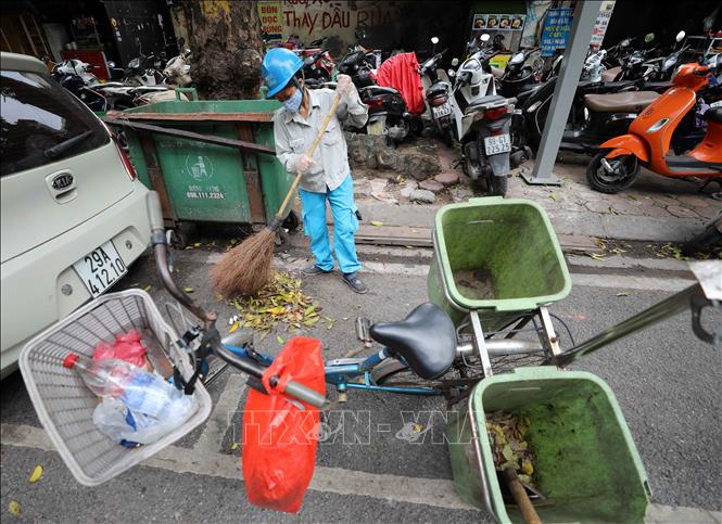 Trong ảnh: Với chiếc xe đạp và vật dụng quen thuộc (chổi, xẻng) người công nhân này đi sau các xe ô tô thu gom rác để làm sạch lần nữa nơi đặt các thùng rác trên phố. Ảnh: Thanh Tùng - TTXVN  