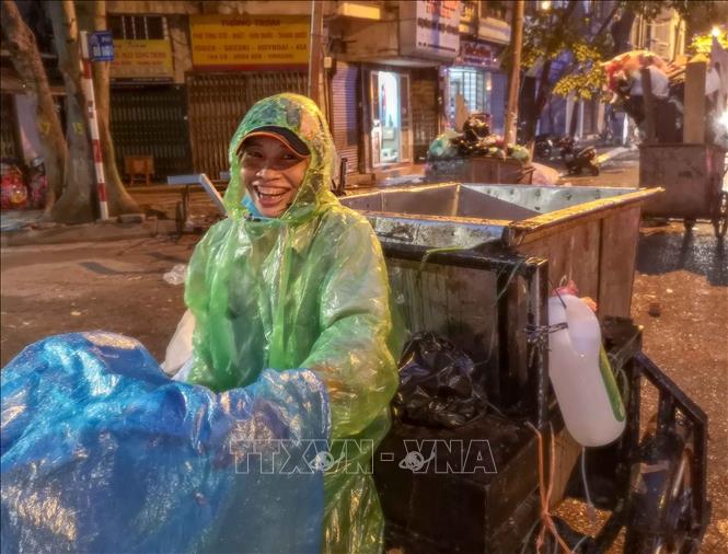 Trong ảnh: Trong mưa gió, người nữ công nhân môi trường vẫn nở nụ nở cười tươi, bởi họ đang góp sức mình để Hà Nội trở nên sạch, đẹp hơn. Ảnh: Thanh Tùng - TTXVN