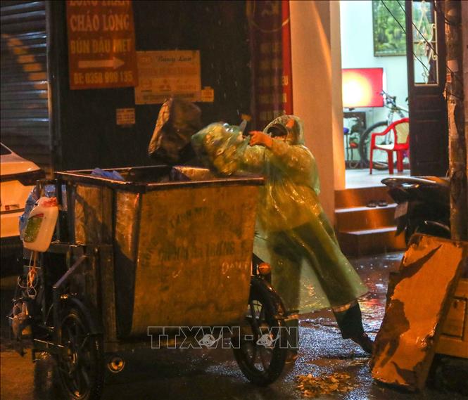 Trong ảnh: Bất kể mưa gió, việc thu gom rác thải của những người làm công tác vệ sinh môi trường vẫn diễn ra bình thường. Ảnh: Thanh Tùng - TTXVN