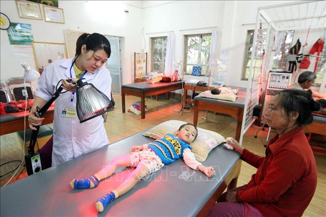 Trong ảnh: Kỹ thuật viên PHCN, điều dưỡng Nguyễn Thị Phương, 28 tuổi, 5 năm công tác đang điều trị cho trẻ em khuyết tật bằng đèn hồng ngoại (ánh sáng trị liệu hay vật lý trị liệu). Ảnh: Anh Tuấn – TTXVN