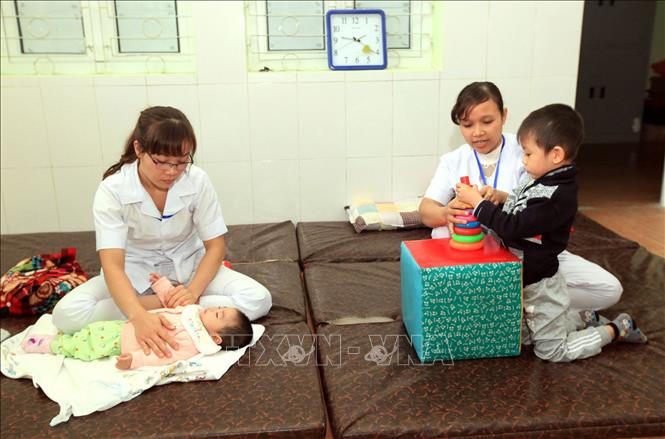 Trong ảnh: Các Kỹ thuật viên PHCN (từ trái sang phải) Nguyễn Hằng Nga, 28 tuổi, 7 năm công tác và Phùng Thị Thúy Nga, 31 tuổi, 9 năm công tác đang tập luyện (tập vận động) cho trẻ bại não. Ảnh: Anh Tuấn – TTXVN