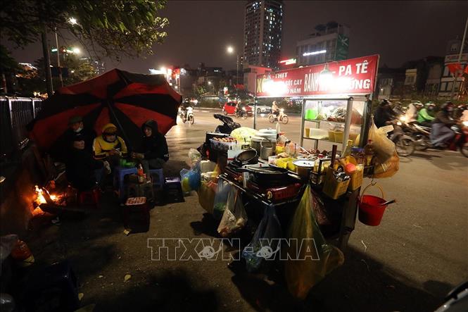 Trong ảnh: Một quán bán hàng rong phải dùng ô che gió và đốt lửa giữ ấm trong đêm lạnh giá buốt. Ảnh: Phan Tuấn Anh - TTXVN