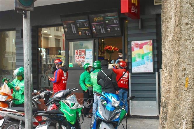 Người dân Hà Nội lựa chọn mua hàng thông qua shipper Grab, Now…để không phải đến tận quán mua hàng. Điều này vừa làm giảm nguy cơ lây nhiễm vì đông người vừa bảo vệ chính người dân. Ảnh: Minh Nghĩa - TTXVN.

