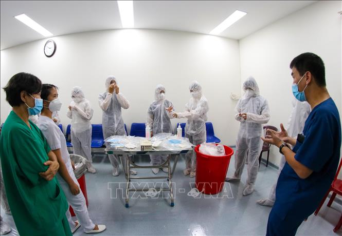 Trong ảnh: Hướng dẫn cho các nhân viên y tế cách mặc đồ bảo hộ đúng cách để đảm bảo an toàn khi tiếp xúc với bệnh nhân tại Bệnh viện dã chiến Tiên Sơn. Ảnh: Trần Lê Lâm - TTXVN

