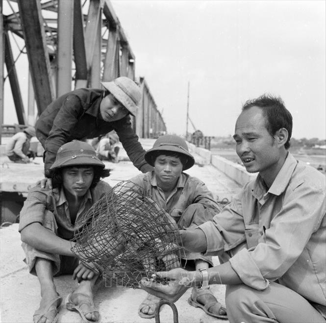 Trong ảnh: Chiến sĩ thi đua Nguyễn Văn Toàn (người không đội mũ), đội trưởng đội 1 xí nghiệp cầu 12 luôn thị sát công việc, tổ chức tốt lao động, đảm bảo tiến độ thi công, xây dựng cầu Chương Dương. Anh đang trao đổi kinh nghiệm làm lưới thép bê tông mặt cầu với anh em trong đội (1985). Ảnh: Bảo Hanh – TTXVN