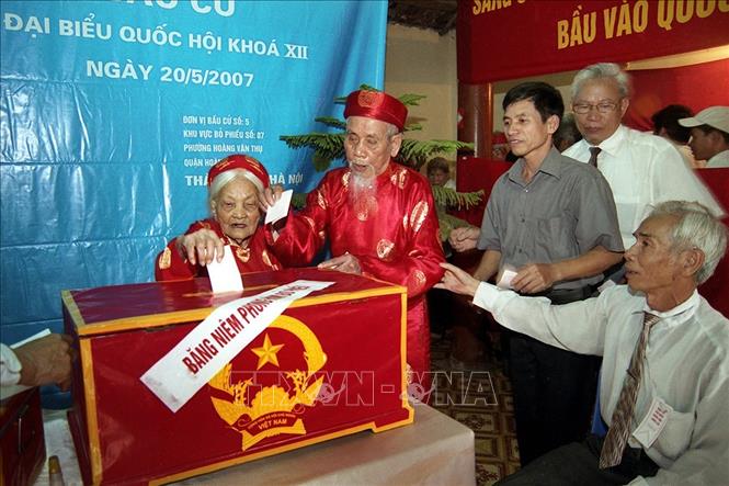 Trong ảnh: Hai cụ Vũ Đình Giả và Ngô Thị Mười tham gia bỏ phiếu (100 tuổi) ở phường Hoàng Văn Thụ, quận Hoàng Mai (Hà Nội) bỏ lá phiếu đầu tiên bầu đại biểu Quốc hội khoá XII tại đơn vị bầu cử số 5, khu vực bỏ phiếu số 7 ngày 20/05/2007. Ảnh: Dương Ngọc-TTXVN