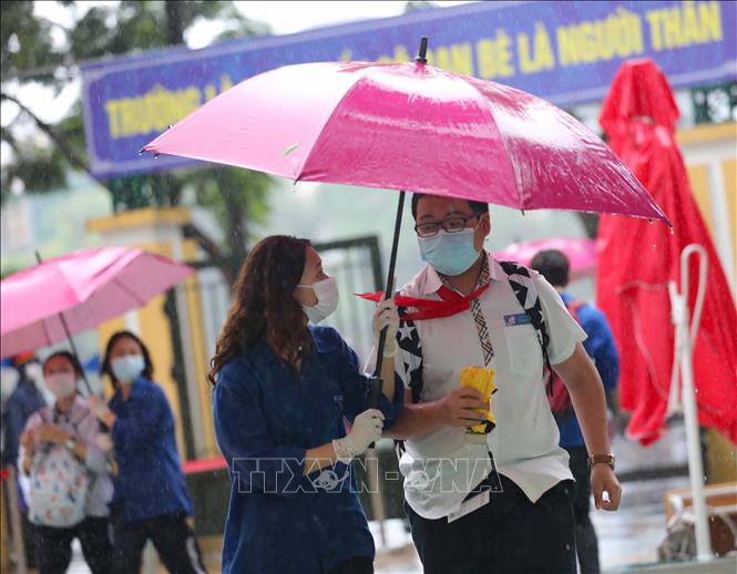 Trong ảnh: Lực lượng tình nguyện che ô tránh mưa và hướng dẫn thí sinh tại điểm thi trường THPT Trần Nhân Tông. Ảnh: Thanh Tùng - TTXVN