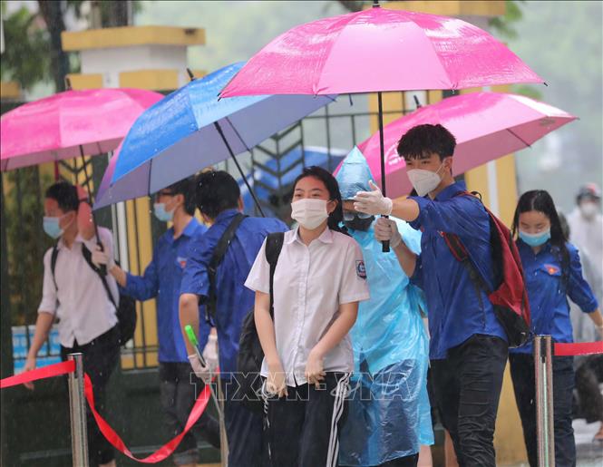 Trong ảnh: Lực lượng tình nguyện che ô tránh mưa và hướng dẫn thí sinh tại điểm thi trường THPT Trần Nhân Tông. Ảnh: Thanh Tùng - TTXVN