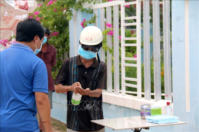 Người dân phải đeo khẩu trang, sát khẩu tay trước khi vào lấy gạo. Ảnh: Nguyễn Thanh - TTXVN