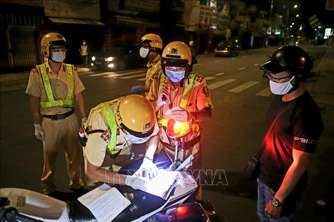 Trong ảnh: Công an lập biên bản xử phạt một trường hợp ra đường không cần thiết sau 18 giờ. Ảnh: Thành Chung - TTXVN