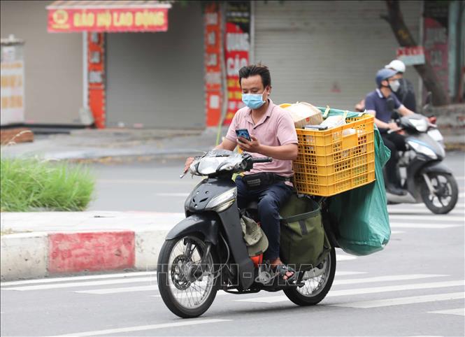 Trong ảnh: Nhân viên giao hàng không đội mũ bảo hiểm lại sử dụng điện thoại khi di chuyển (ảnh chụp chiều 10/8/2021). Ảnh: Thanh Tùng - TTXVN