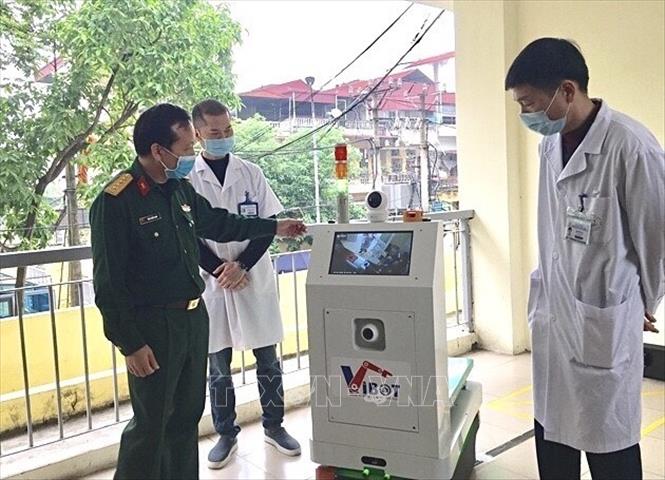 Trong ảnh: VIBOT-1 gồm 1 Trung tâm giám sát, điều khiển và 1 robot di chuyển theo đường dẫn có từ tính, nhằm hỗ trợ, thay thế một phần nhân viên y tế và tạp vụ trong một không gian hạn chế có nguy cơ lây nhiễm cao, đặc biệt là khu vực cách ly với dịch COVID-19  (VIBOT-1 với các bác sĩ bệnh viện Bắc Thăng Long, tháng 4/2020). Ảnh: TTXVN phát 
