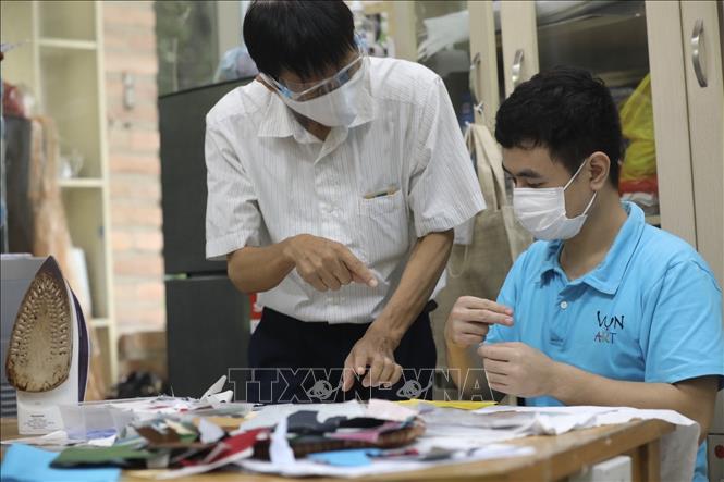 Trong ảnh: Thầy giáo hướng dẫn bằng ký hiệu riêng cho người lao động khuyết tật tạo ra các sản phẩm mới. Ảnh: Minh Quyết - TTXVN