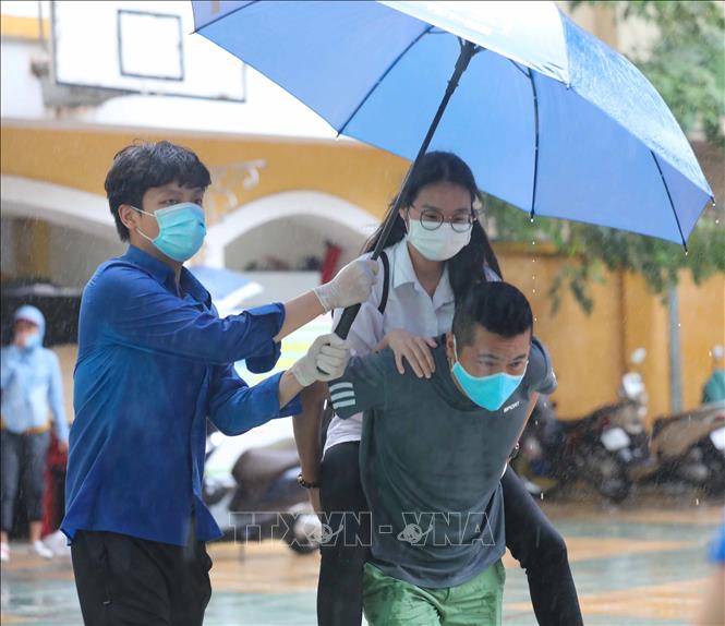 Trong ảnh: Tình nguyện viên che ô tránh mưa cho thí sinh bị đau chân tại điểm thi trường THPT Trần Nhân Tông (Hà Nội) trong kỳ thi tuyển sinh vào lớp 10 THPT công lập năm học 2021 - 2022. Ảnh: Thanh Tùng – TTXVN

