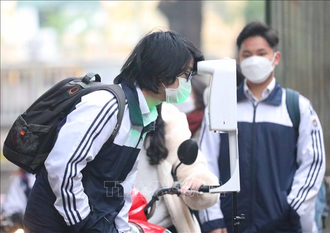 Các em học sinh đo thân nhiệt, sát khuẩn tay khi tới trường. Ảnh: Thanh Tùng - TTXVN 