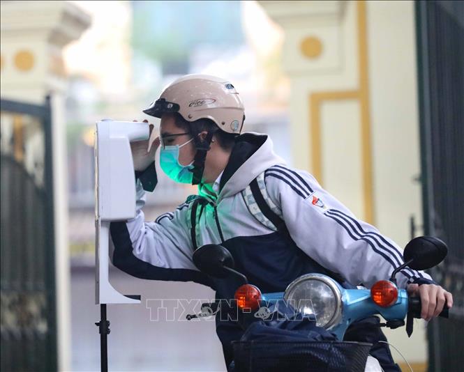 Các em học sinh đo thân nhiệt, sát khuẩn tay khi tới trường. Ảnh: Thanh Tùng - TTXVN 