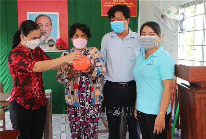 Bà Huỳnh Thị Lệ, Chi hội trưởng Chi hội phụ nữ ấp Đồng Khoen, xã Phong phú, huyện Cầu Kè (bên trái) trao heo đất cho hội viên phụ nữ tham gia mô hình. Ảnh: Thanh Hòa - TTXVN