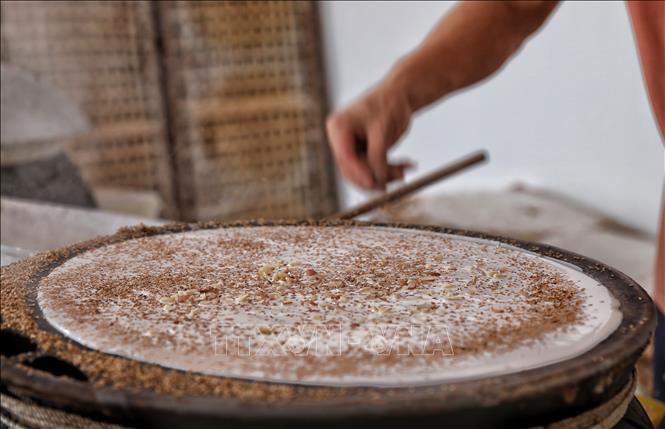 Vừng và lạc sống đã giã dập được rắc lên bánh trong khi tráng. Ảnh: Danh Lam-TTXVN