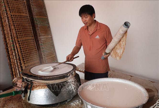 Khi bánh đã được tráng chín, người ta khéo léo dùng một ống to, dài quấn lớp bánh quanh ống lấy ra khỏi nồi hơi để mang trải đều trên phên. Ảnh: Danh Lam-TTXVN