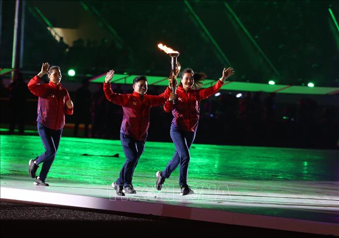 Cựu vô địch SEA Games Nguyễn Thị Tĩnh (trái) cầm đuốc từ phía ngoài SVĐ quốc gia Mỹ Đình chạy vào phía trong sân, trao lại cho bộ đôi cựu VĐV Trần Lê Quốc Toàn (cử tạ - giữa), Lê Bích Phương (karate - phải) tiếp tục chạy để đưa ngọn đuốc vào trong sân. Ảnh: TTXVN