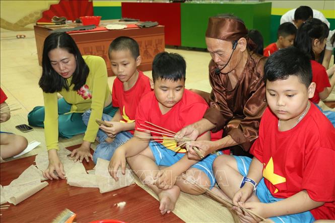Trong ảnh: Các thợ làng nghề của làng Nam hướng dẫn học sinh làm quạt giấy. Ảnh: Bích Huệ - TTXVN