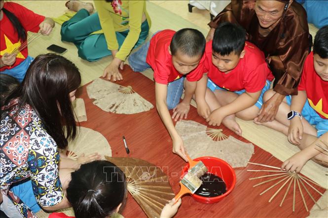 Trong ảnh: Các thợ làng nghề của làng Nam hướng dẫn học sinh làm quạt giấy. Ảnh: Bích Huệ - TTXVN