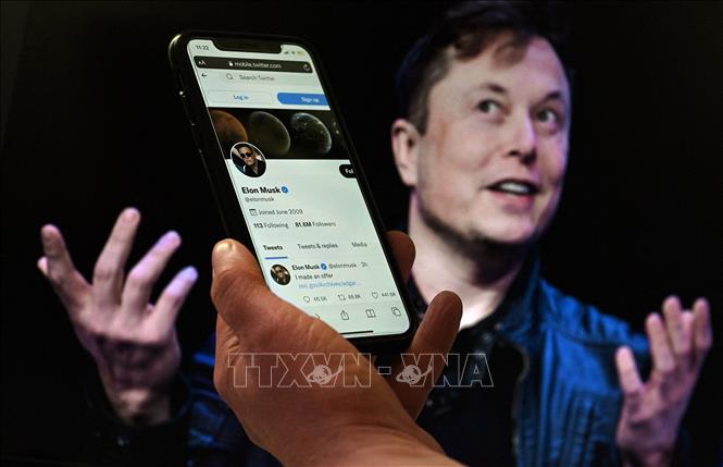 Trong ảnh: Tài khoản Twitter của tỷ phú Elon Musk trên màn hình điện thoại và ảnh chụp ông Musk (phía sau) tại một sự kiện ở Washington, DC, Mỹ ngày 14/4/2022. Ảnh: AFP/TTXVN