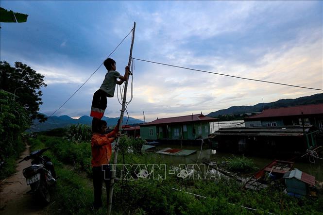 Trong ảnh: Hai bố con đang kéo lại đường dây điện để thắp sáng khi thủy điện Hòa Bình mở cửa xả lũ đầu tiên ngày 12/6/2022 làm nước sông Đà dâng cao gây chia cắt các hộ và xảy ra các sự cố về dây điện tại làng vạn chài. Ảnh: Trọng Đạt-TTXVN 