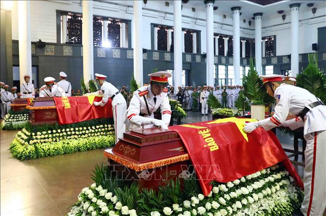 Thực hiện nghi thức phủ Cờ Bảo vệ An ninh Tổ quốc lên linh cữu 3 liệt sĩ. Ảnh: Phạm Kiên - TTXVN