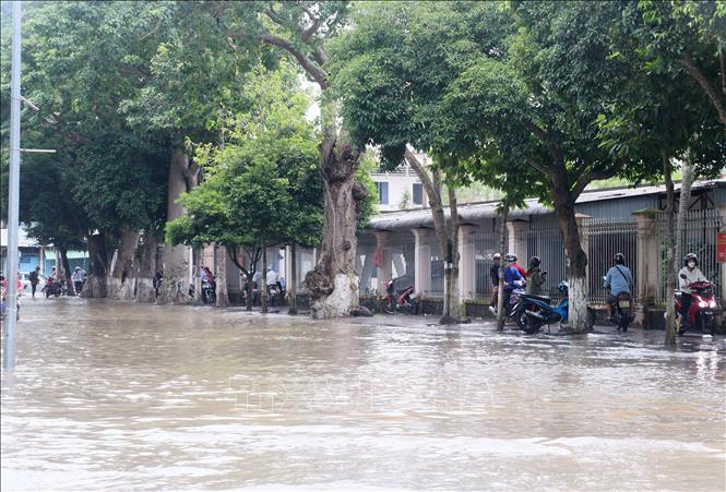 Trong ảnh: Triều cường dâng cao gây ngập đường, khiến nhiều người dân phải cho xe máy lên vỉa hè chờ nước rút. Ảnh: Lê Thúy Hằng - TTXVN