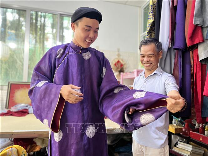 Ông Trần Thanh Tòng ướm thử đồ cho khách. Ảnh: Ánh Tuyết - TTXVN