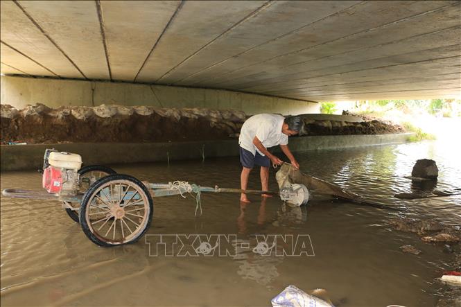 Trong ảnh: Đoạn đường dưới cầu Xáng Nhỏ bị ngập nước, nên ông Dương Văn Thố (người dân xã Bình Thạnh Trung) thường xuyên phải dùng máy bơm của gia đình để bơm nước ra ngoài. Ảnh: Nhựt An - TTXVN