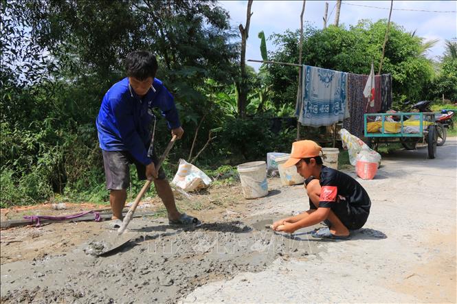 Trong ảnh: Anh Nguyễn Văn Khâm cùng con trai cần mẫn vá những “ổ voi”, “ổ gà” trên đường. Ảnh: Nhựt An - TTXVN