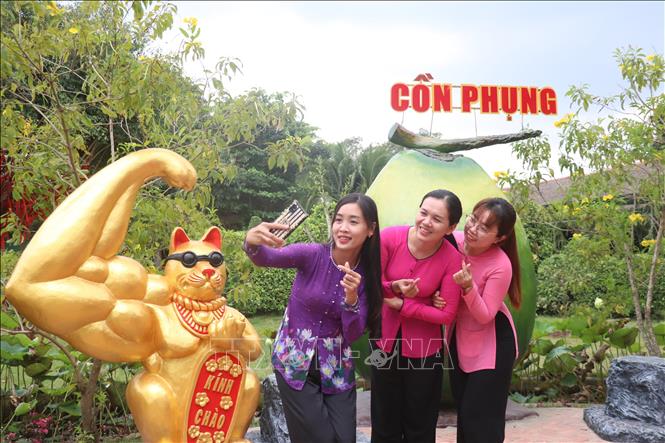 Khách du lịch thích thú chụp ảnh với linh vật “Mèo lực sĩ”. Ảnh: Huỳnh Phúc Hậu - TTXVN