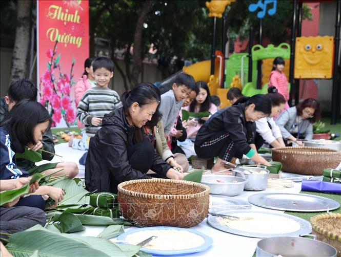 Các mẹ, các con cùng nhân viên của làng gói bánh chưng tết. Ảnh: Hoàng Hiếu - TTXVN 