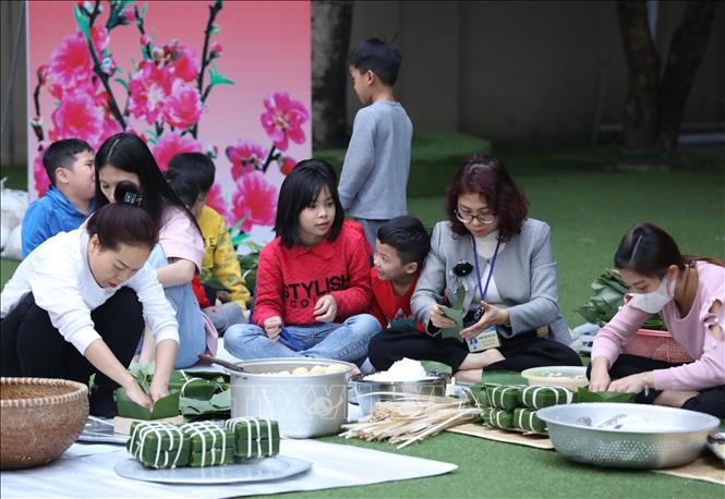 Các mẹ, các con cùng nhân viên của làng gói bánh chưng tết. Ảnh: Hoàng Hiếu - TTXVN 